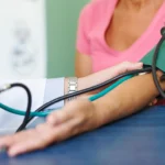 Profesional de la salud midiendo la presión arterial de una paciente mayor con un tensiómetro manual durante un chequeo preventivo.